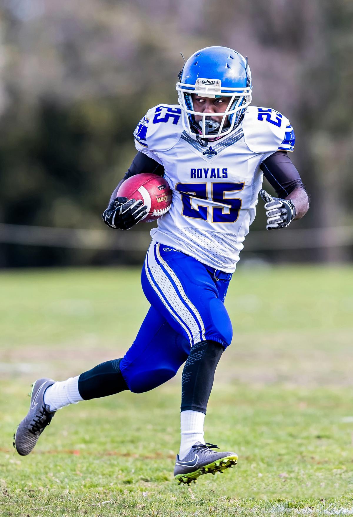 A football player in a running back position, with the ball tucked under his right arm while looking to his left.