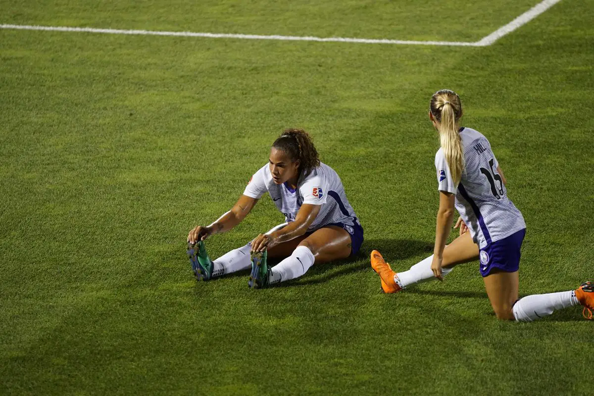 A group of women soccer players holding the ball in a soccer field.